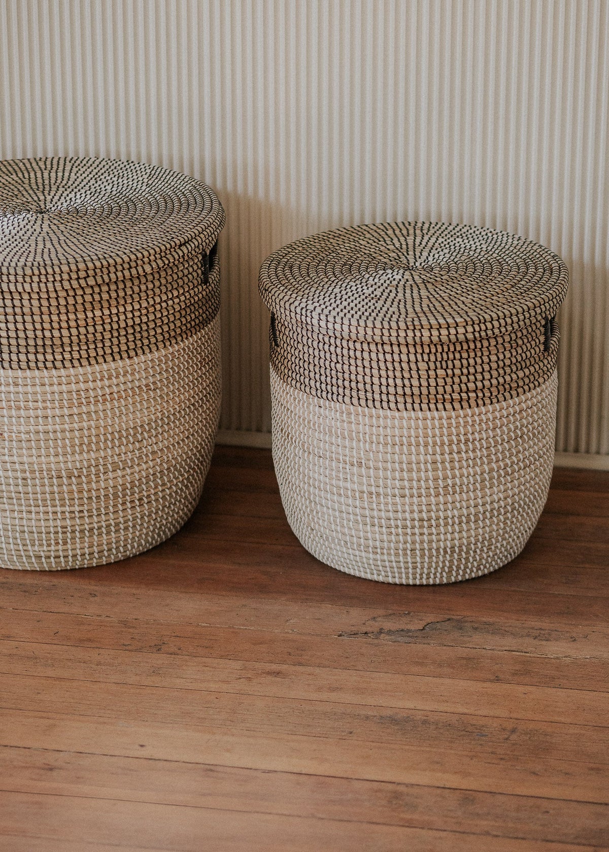 Large and small lidded baskets displayed side by side against a softly striped wall.