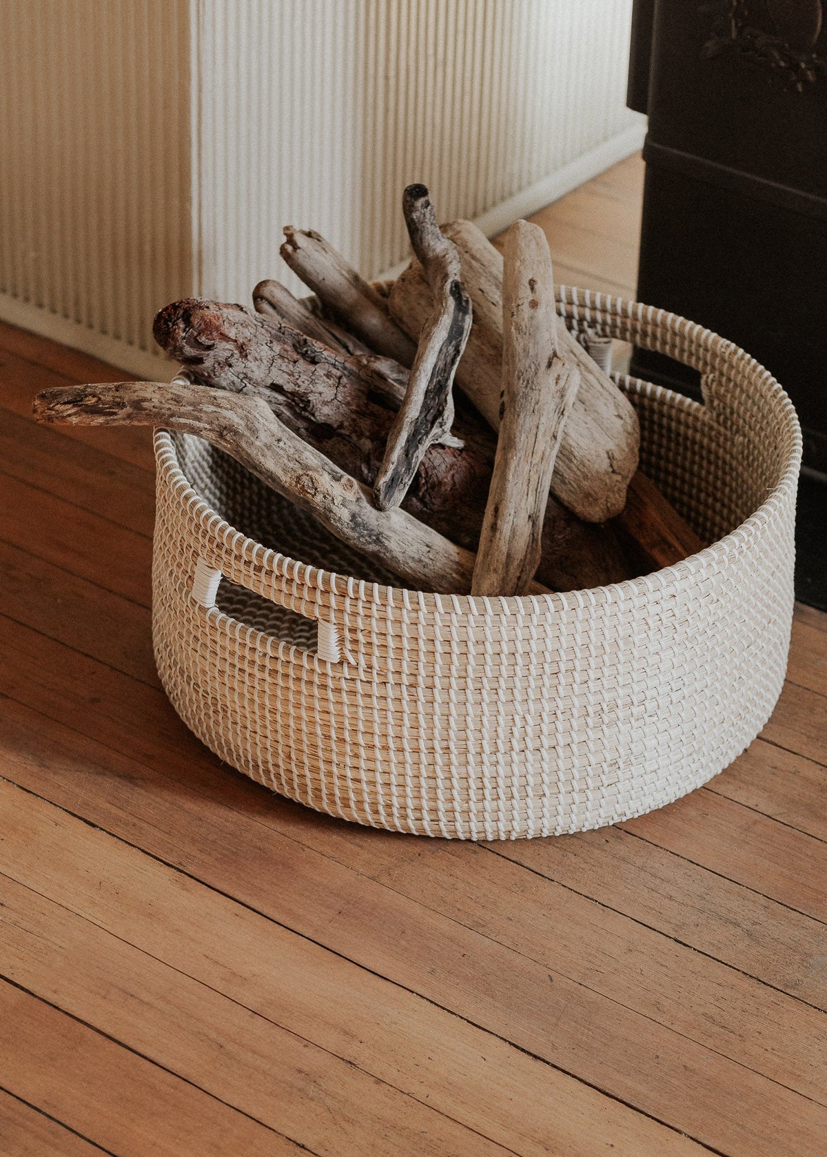 Close view of the seagrass basket holding split logs on a warm wood floor.