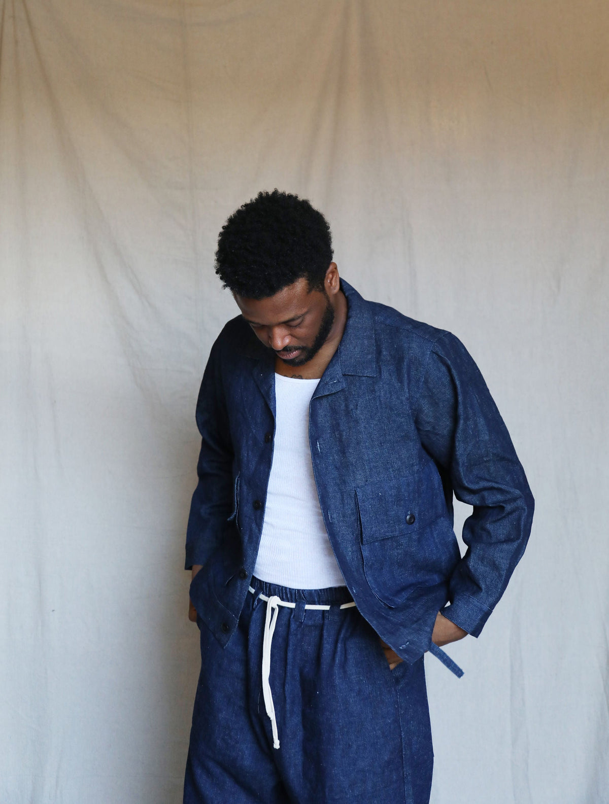 Model looking down while wearing the indigo Studio Coat over a white shirt and matching pants.