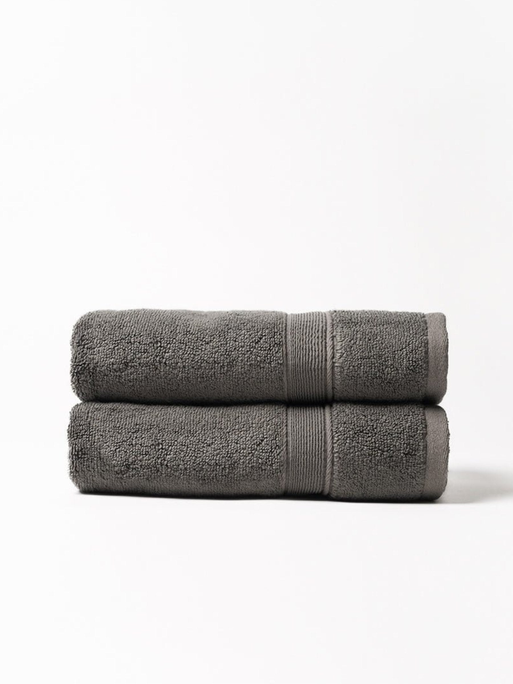Two charcoal gray bath towels folded and stacked on a white background, showing plush looped fabric and matching woven border bands.