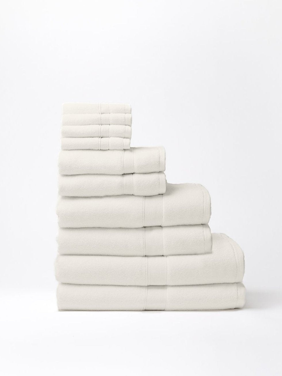 Ivory towels stacked by size on a white background, with small washcloths at the top and larger bath towels at the base, showing plush texture and woven border bands.