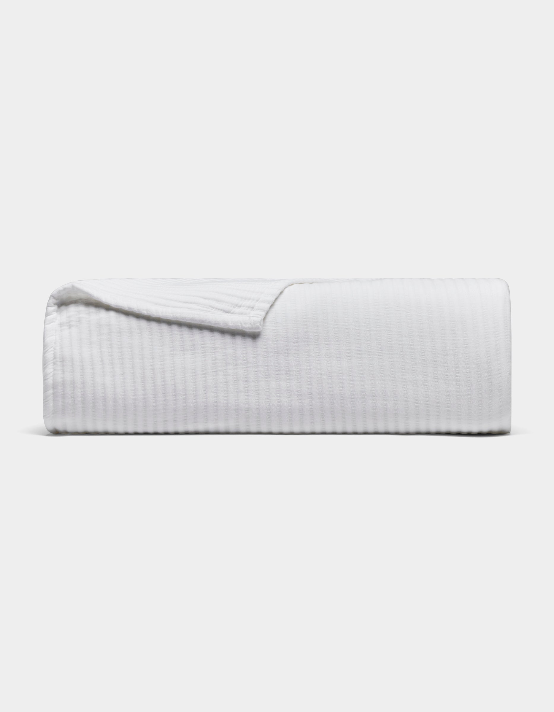 White Bamboo Coverlet folded on a pale background, with one corner turned back to reveal its fine ribbed texture and stitched edge.