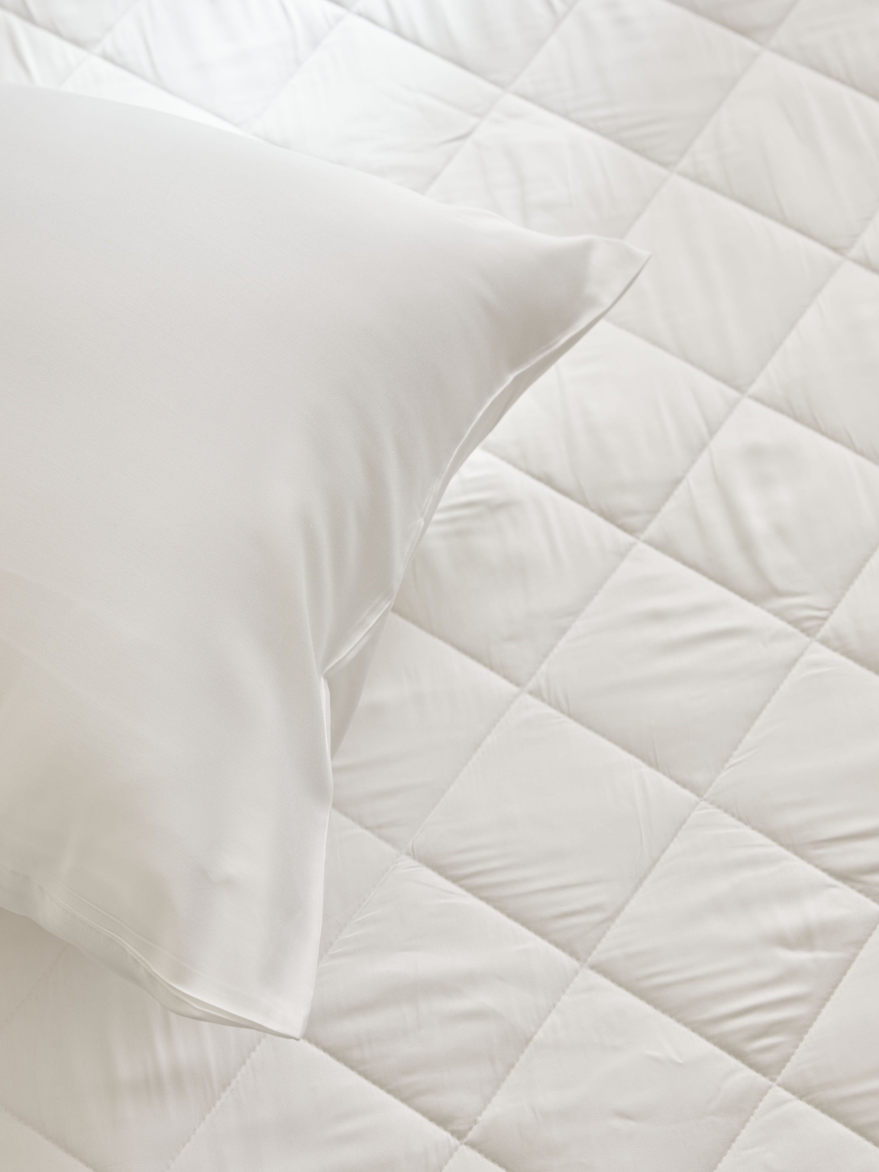 Overhead close-up of a white pillow resting on the mattress pad, showing its diamond-pattern stitching and gently cushioned surface.
