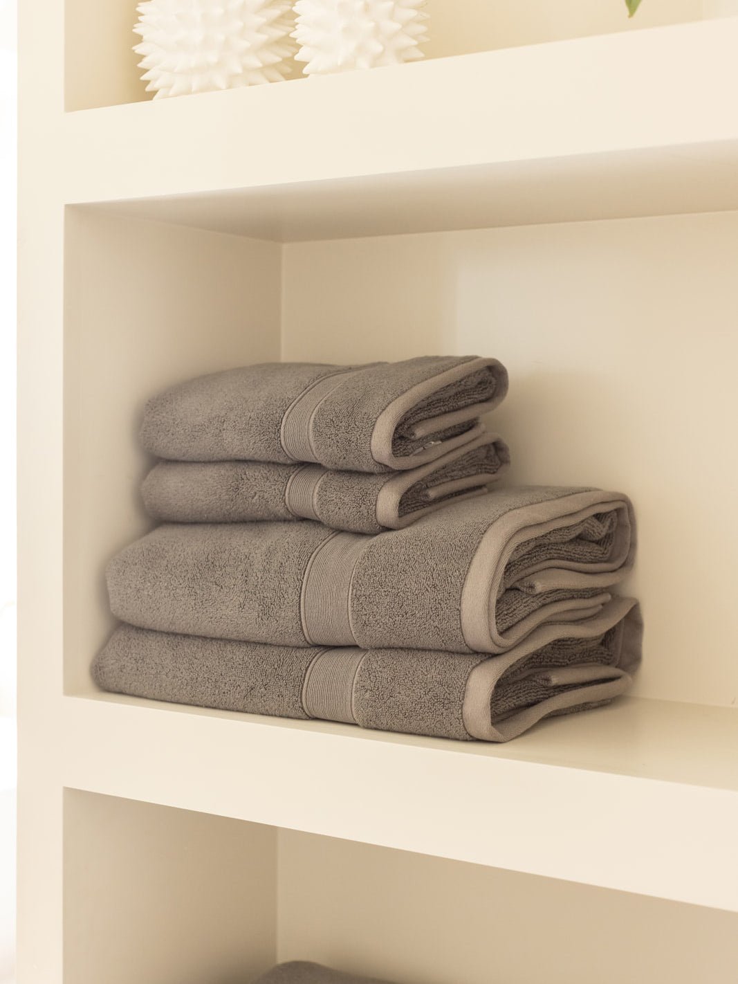 Charcoal gray towels stacked on a cream shelf, with smaller folded towels resting on two larger towels and their rolled edges facing outward.