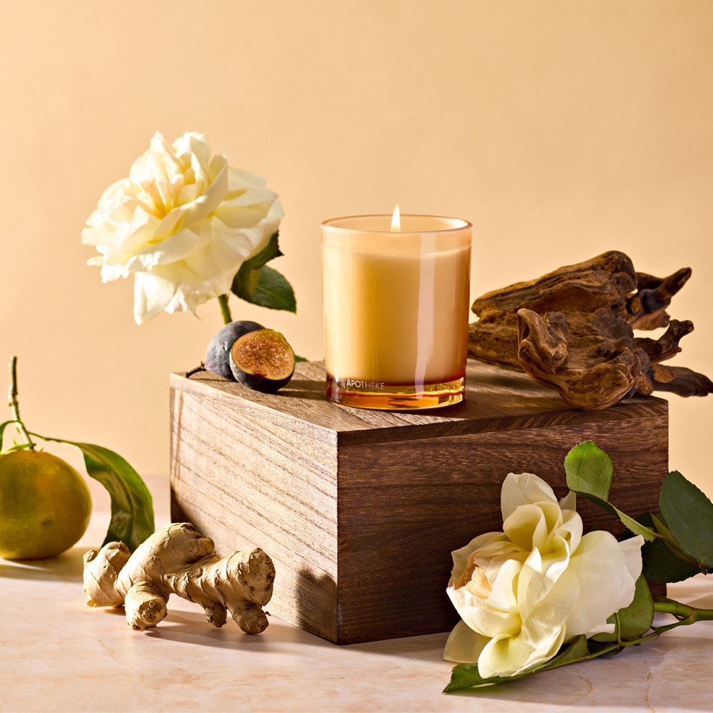 APOTHEKE Cedarwood Ginger Petite Candle styled on a wood block with white flowers, ginger root, and a pear