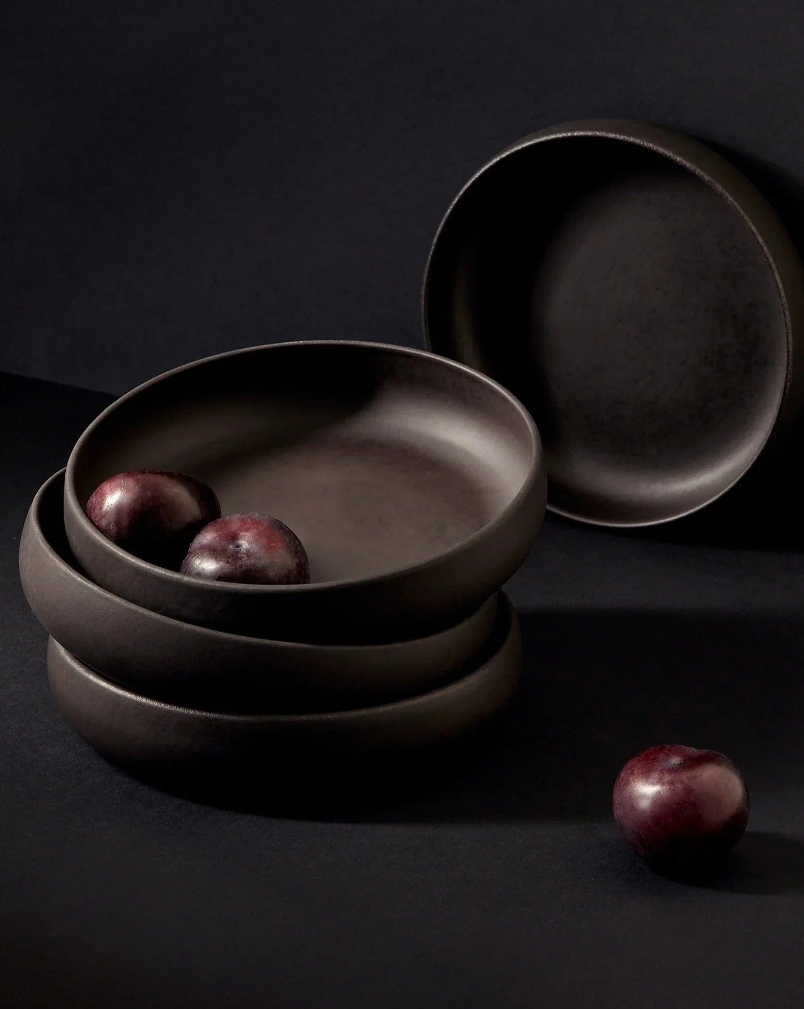 Stoneware pasta bowls in Matte Black stacked with plums on dark background