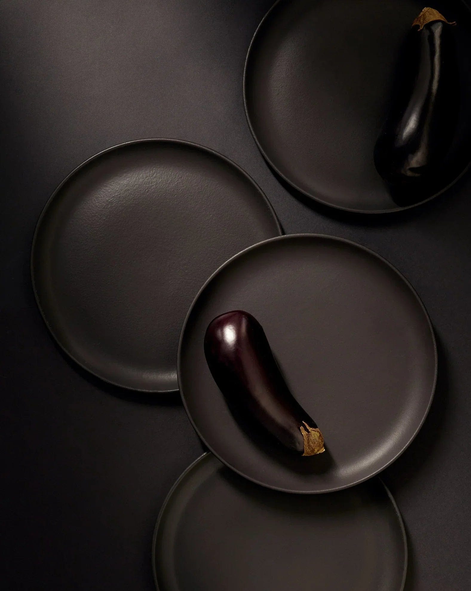 Stoneware dinner plates in Matte Black overhead view with eggplant on dark background