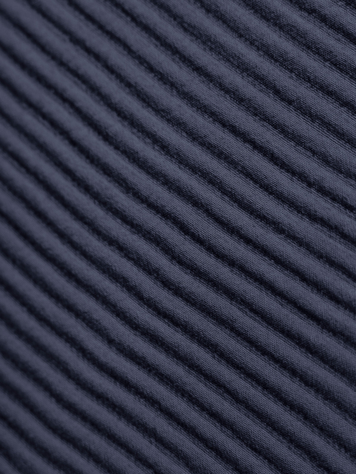 Close-up of the navy coverlet’s fabric, showing closely spaced raised ribs running diagonally across the image.