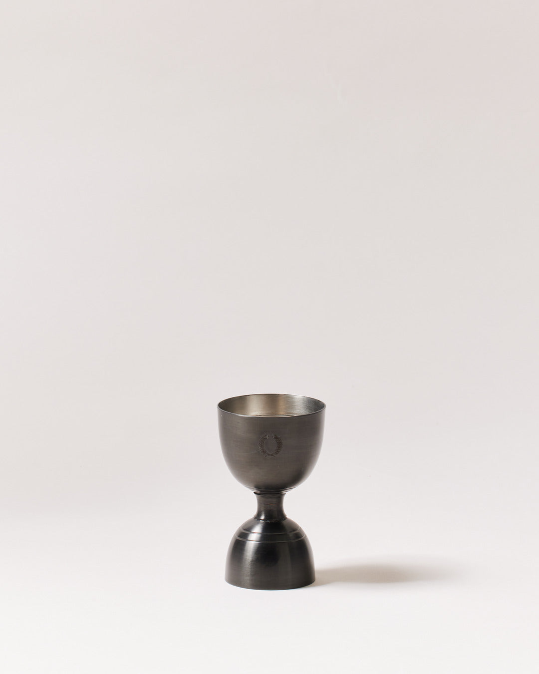 Double-sided brushed-onyx jigger standing upright with dark exterior cups and a contrasting silver interior.