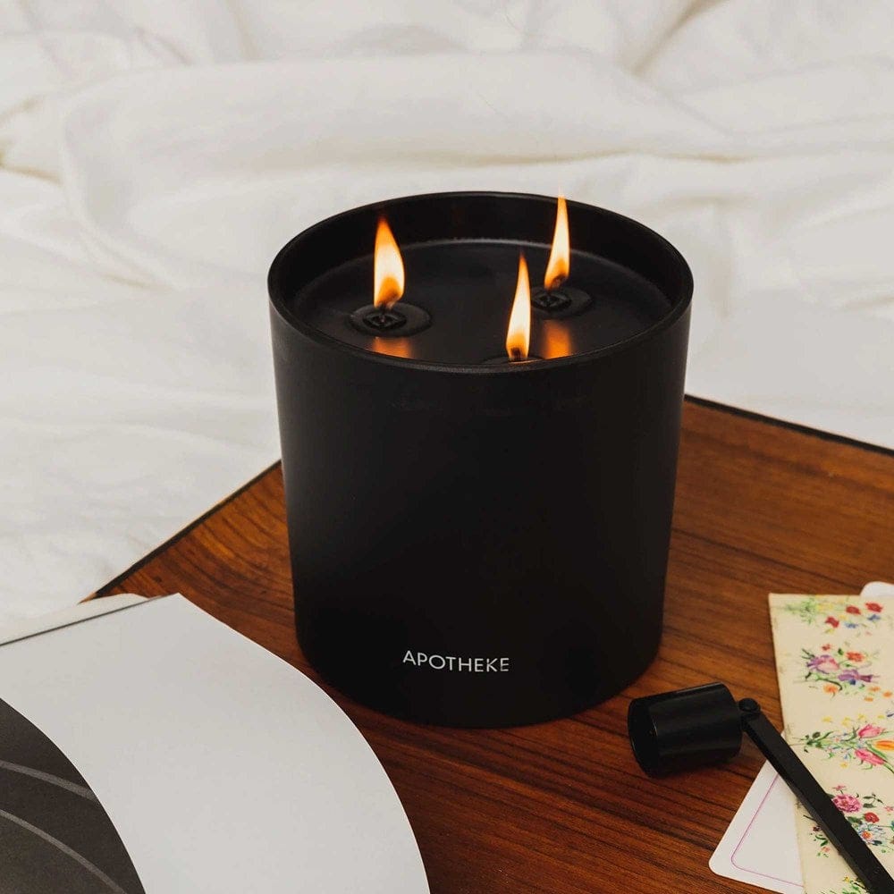 Lit Charcoal APOTHEKE 3-Wick Candle on a wood tray with white linen and a wick trimmer nearby