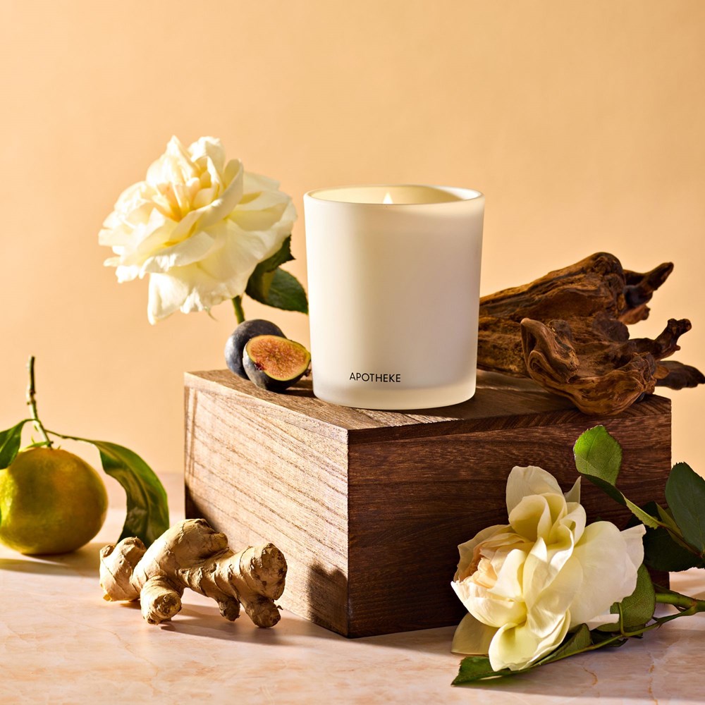 APOTHEKE Cedarwood Ginger Classic Candle styled on a wood block with white flowers, figs, and fresh ginger root