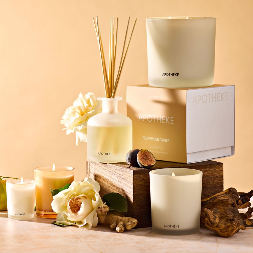 APOTHEKE Cedarwood Ginger Classic Candle displayed with matching reed diffuser, votive candle, and white flowers in a styled vignette