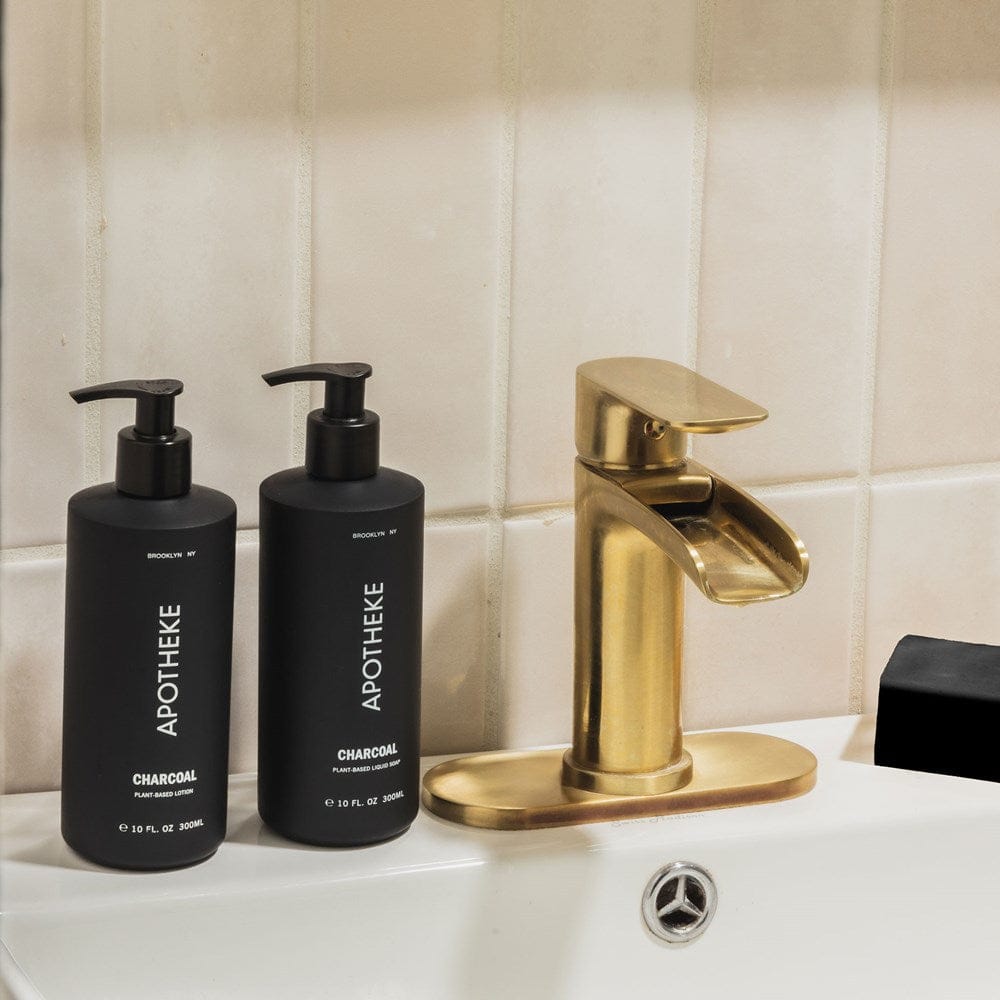 APOTHEKE Charcoal Lotion and Liquid Soap bottles styled on a bathroom sink beside a gold faucet