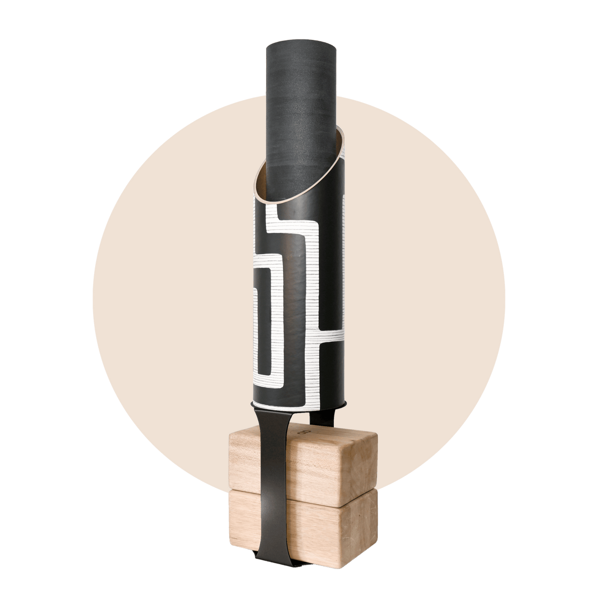 Black cylindrical yoga mat tube with a bold white maze pattern, holding a rolled black mat and standing on four pale wood blocks with a black support strap.