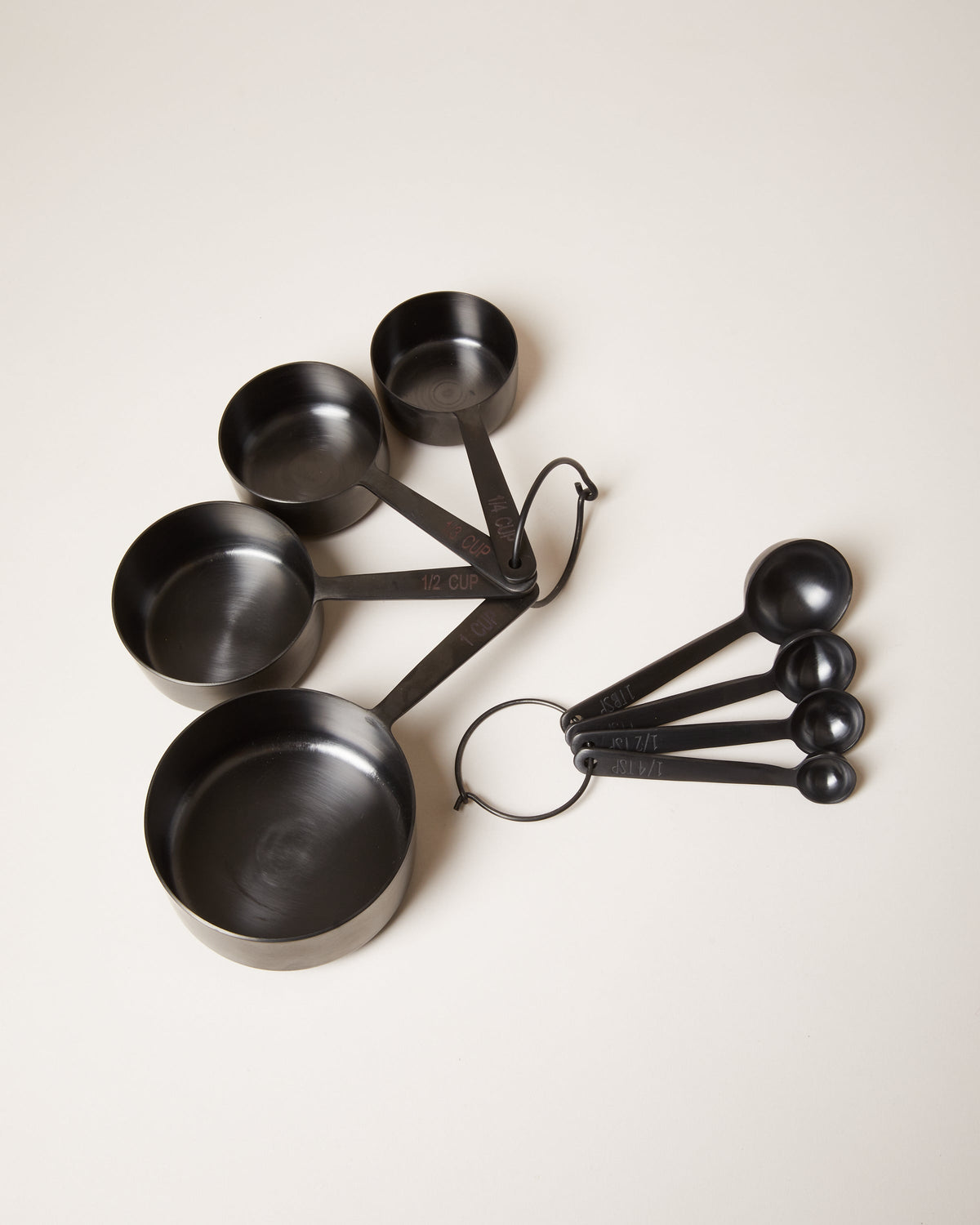 Coordinating matte black measuring cup and measuring spoon sets fanned across a pale neutral background.