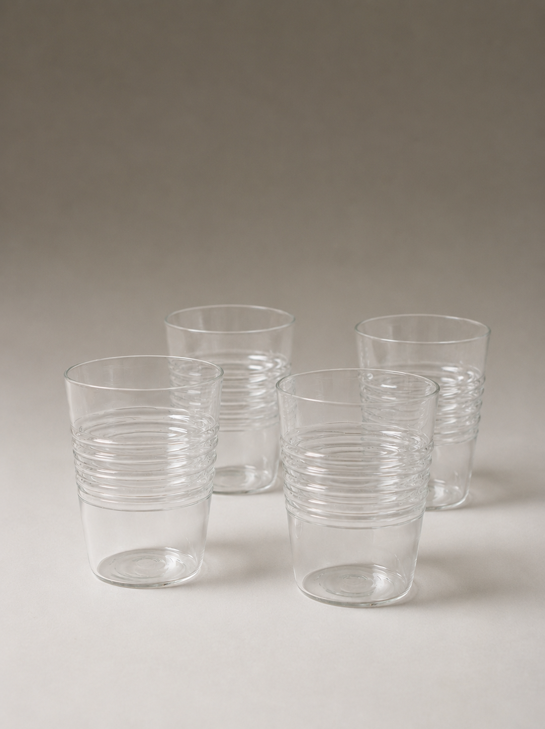 Five clear ridged tumblers grouped together against a softly lit neutral background.