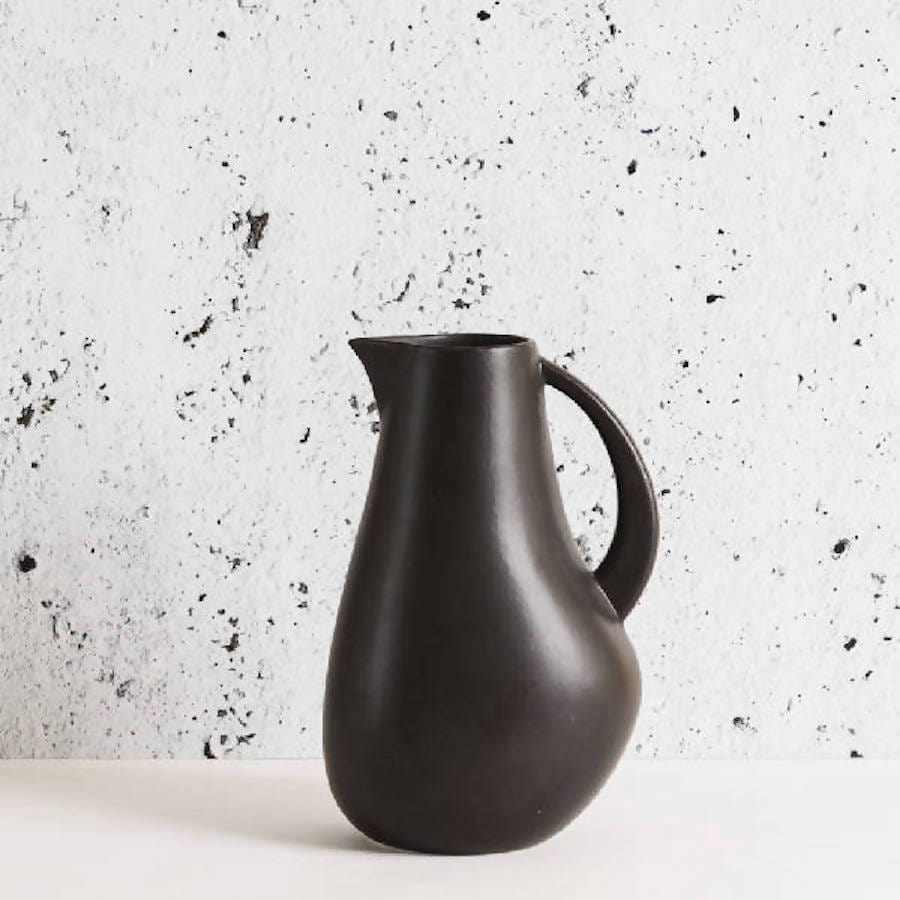 Stoneware pitcher 64 oz in Matte Black against textured concrete background