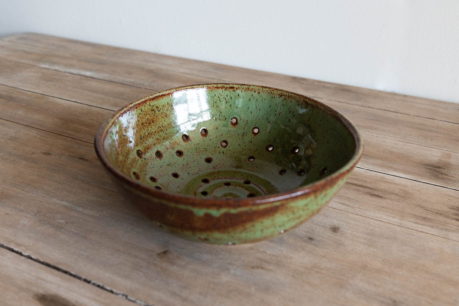 Green ceramic colander with brown accents on a wooden surface