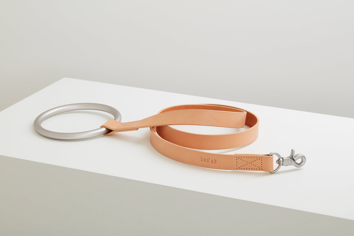 Coiled peach Lumi Leash displayed on a raised white platform with its large silver ring handle and polished metal clasp visible.