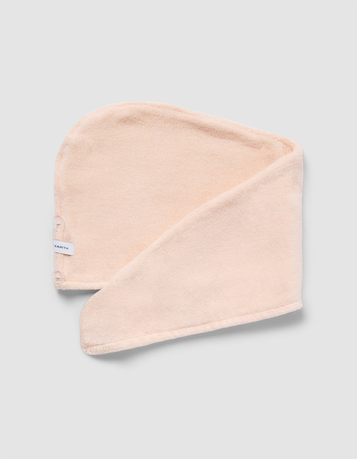 Pale peach hair towel displayed flat with an overlapping fold, showing its rounded shape, textured surface, and finished edge.