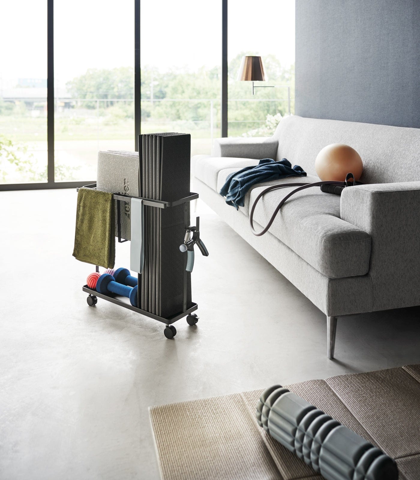 Modern living room with a gray sofa, exercise ball, and a rolling cart with fitness equipment.