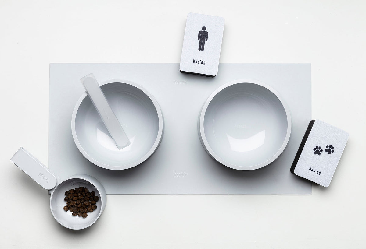 Overhead view of the two labeled sponges arranged with pale pet bowls, feeding spoons, and a small bowl of dry food to show their separate uses.