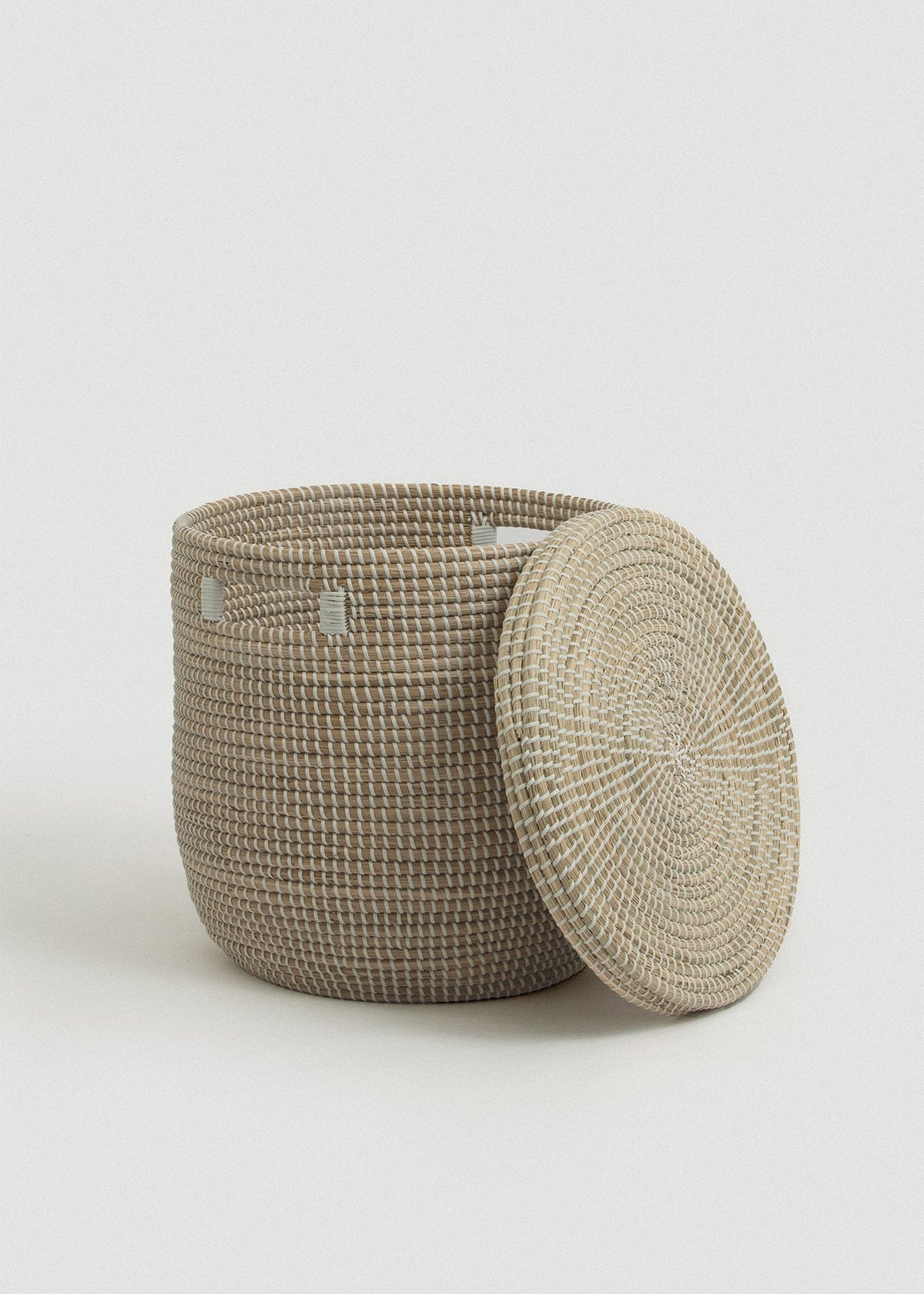 Open seagrass basket with the flat circular lid leaning against its side.