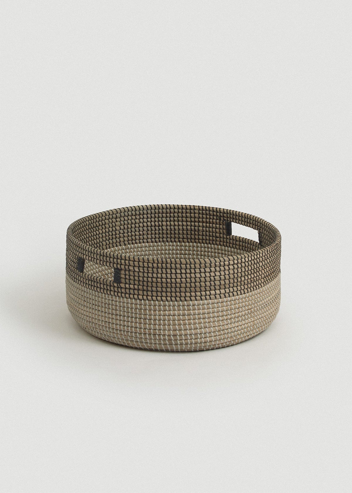 Low round seagrass floor basket with a natural base, black upper band, and two rectangular cutout handles.