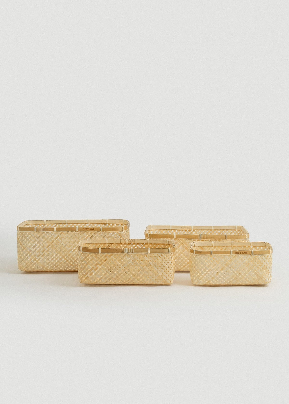 Set of four natural woven bamboo organizing baskets in graduated rectangular sizes.