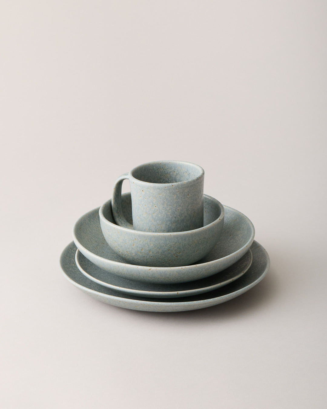 Complete blue-gray speckled place setting with a mug, bowl, and three graduated plates stacked against a pale neutral background.