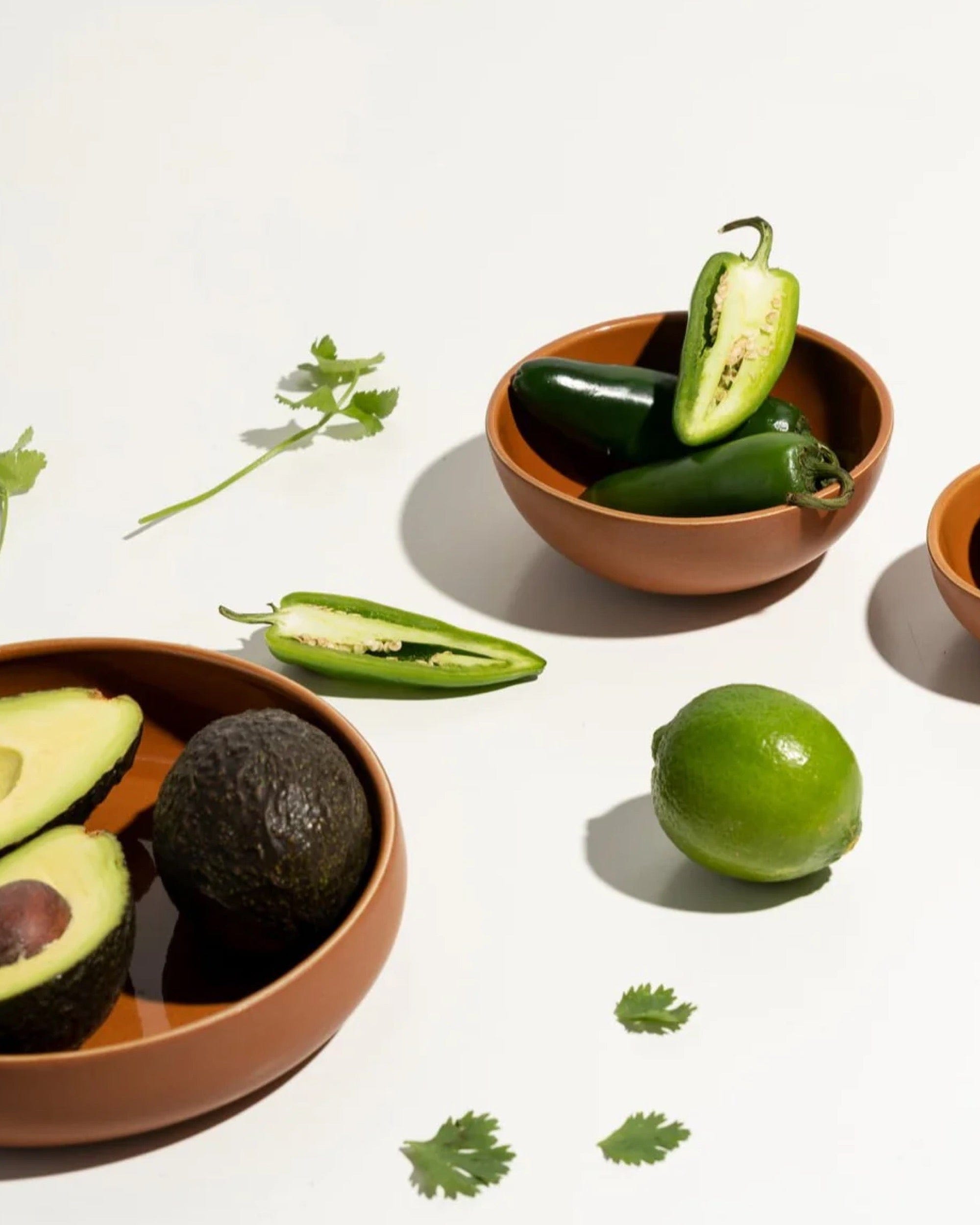 Stoneware bowl in Terracotta styled overhead with avocado, lime, and herbs