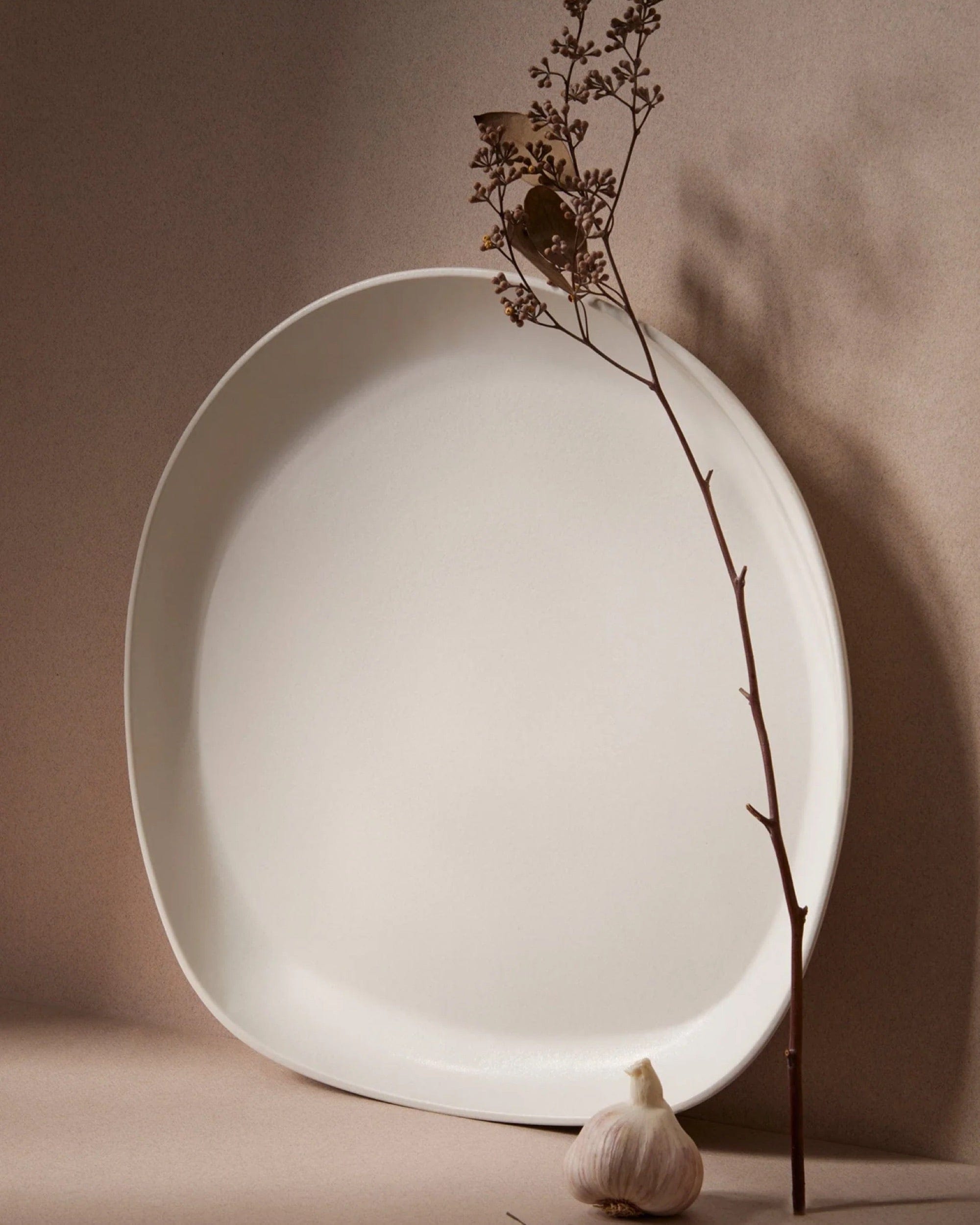 Stoneware round serving platter in Matte White with dried branch and garlic