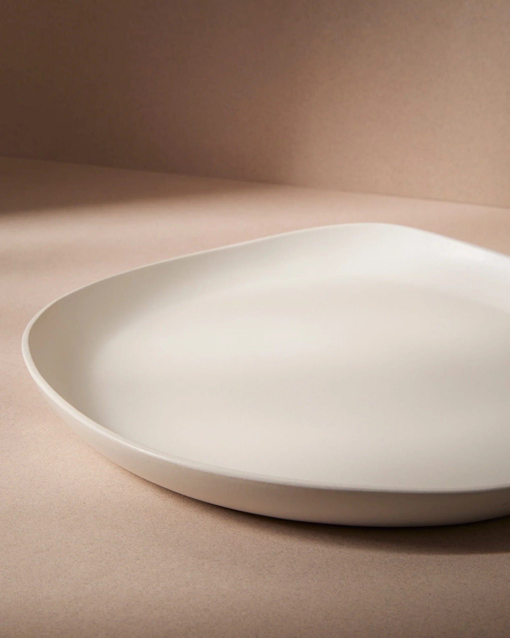 Stoneware round serving platter in Matte White angled view on warm-toned background