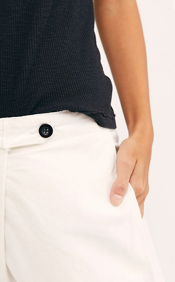 Close-up of the white Souk pants showing the black front button, waistband, and side pocket.