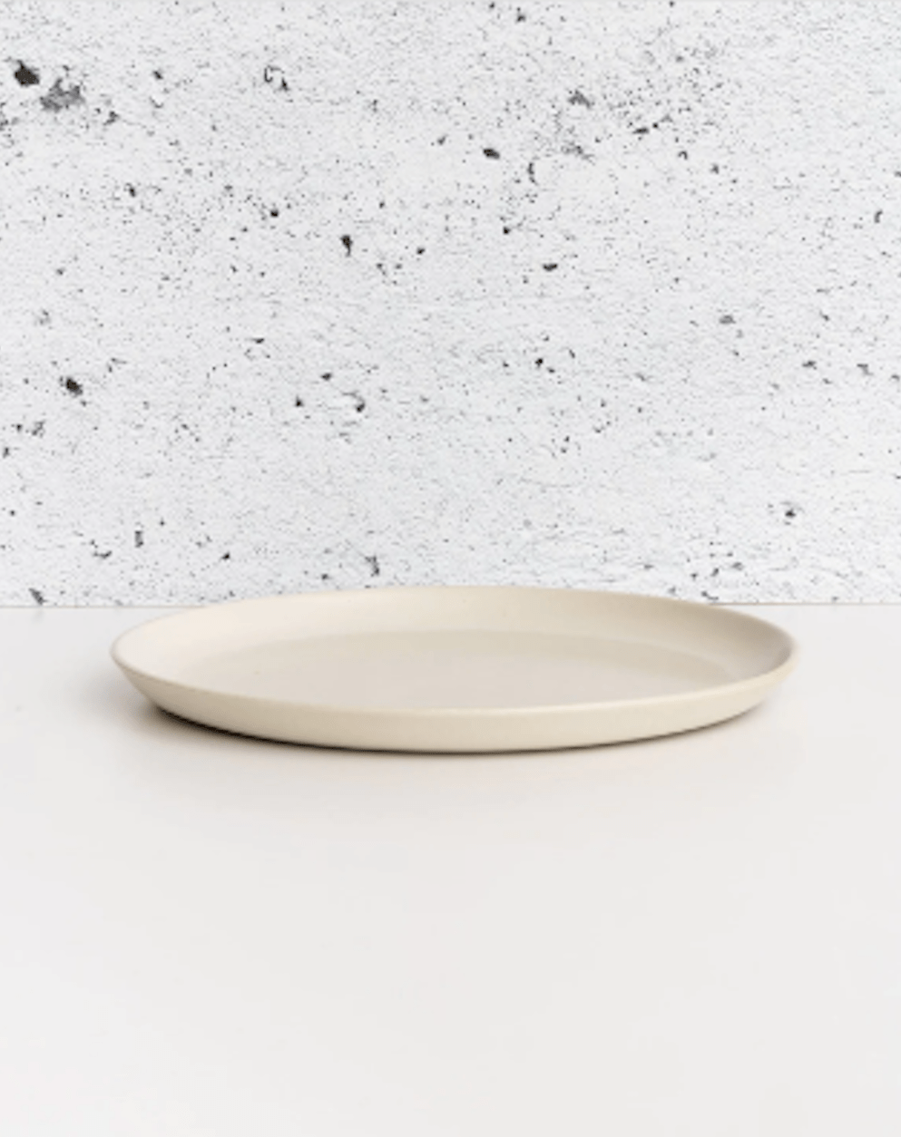 Stoneware dinner plate in Matte White side profile view against textured concrete background