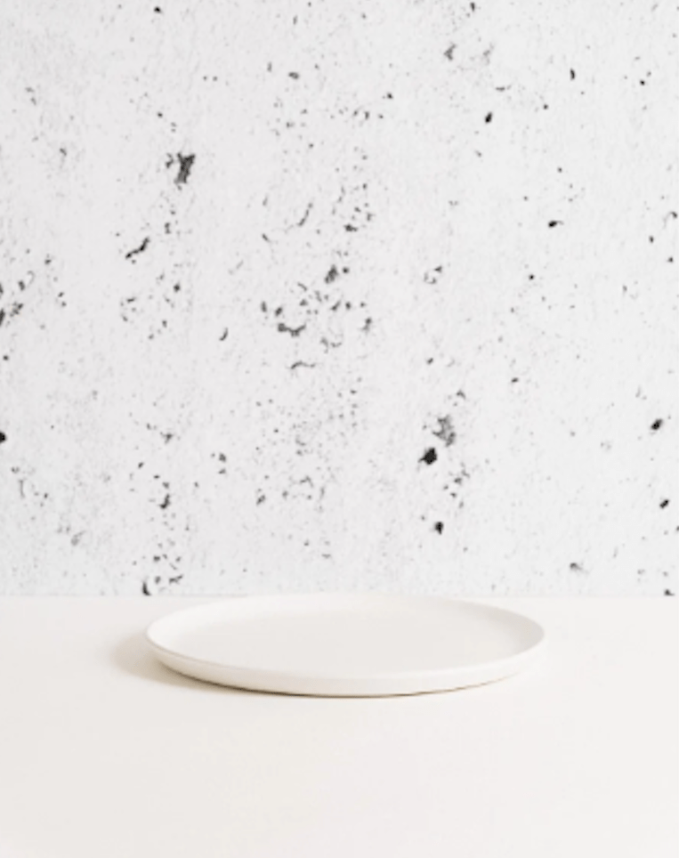 Stoneware side plate in Matte White side profile view against textured concrete background