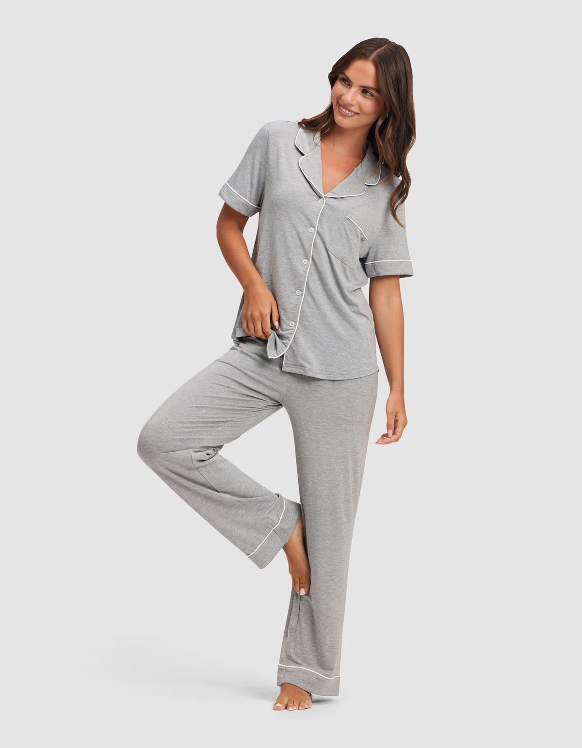 Front view of the light gray pajama set on a model posing with one knee raised, showing the chest pocket, white trim, and relaxed pant legs.