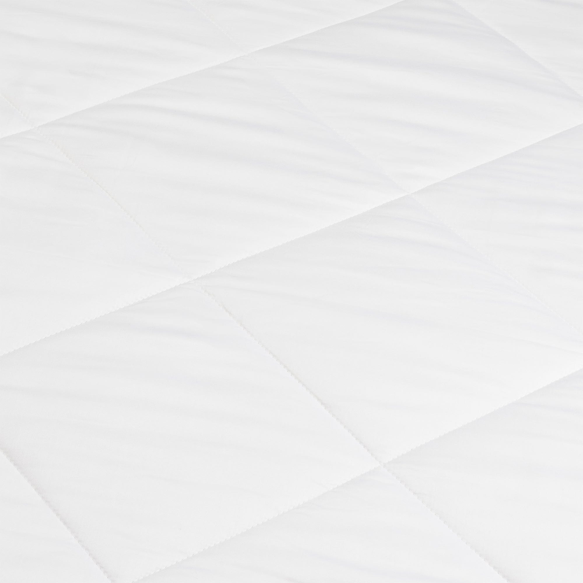Detail of the white comforter’s gently rippled surface, with diagonal seams dividing the fabric into large quilted sections.