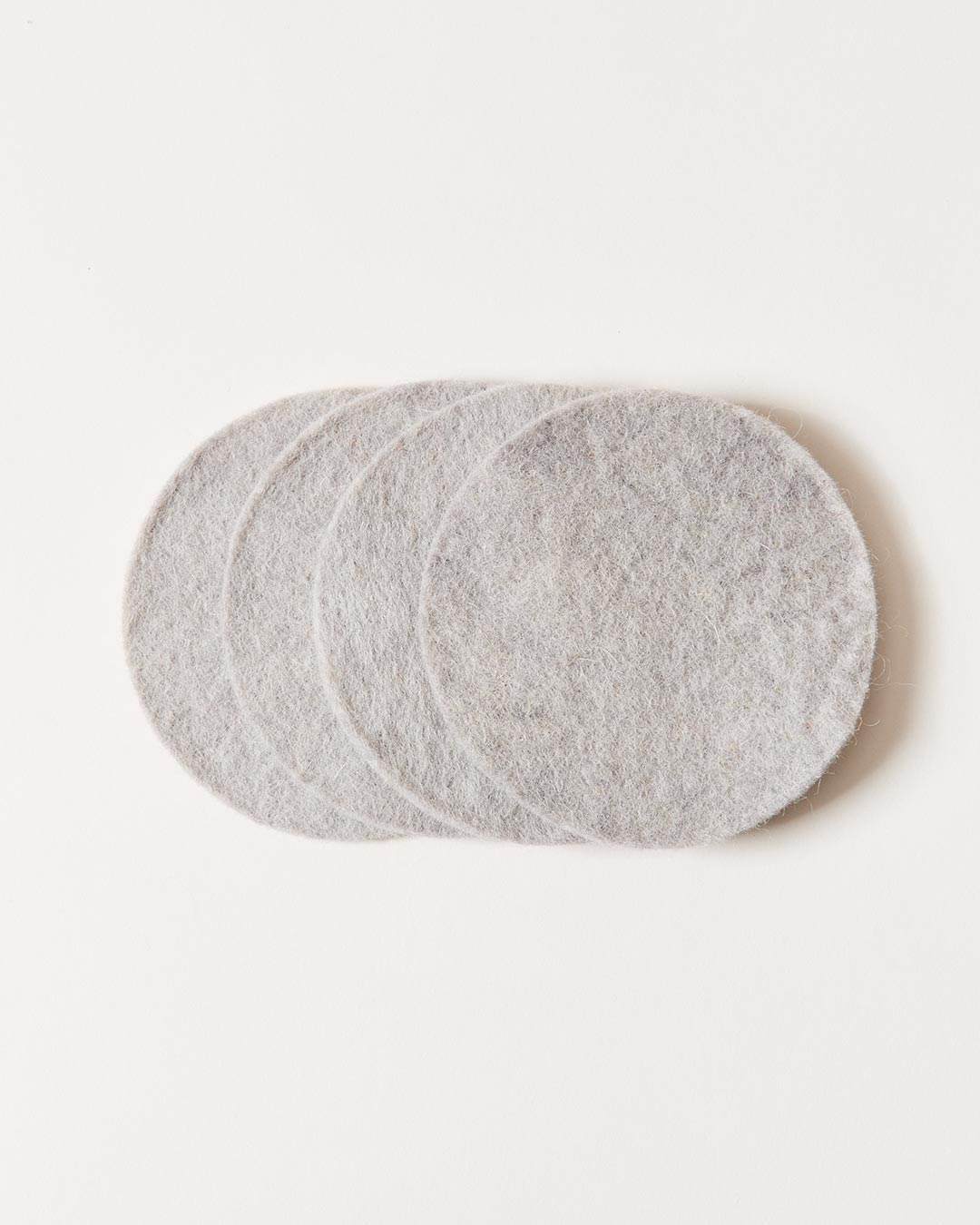 Stack of pale gray felt coasters arranged in an overlapping fan, showing their smooth circular shape and softly mottled fibers.