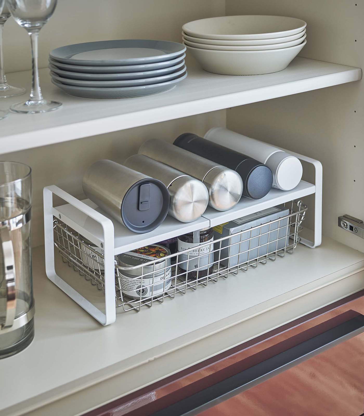 Kitchen shelf with storage rack holding tumblers and a basket, above a countertop.