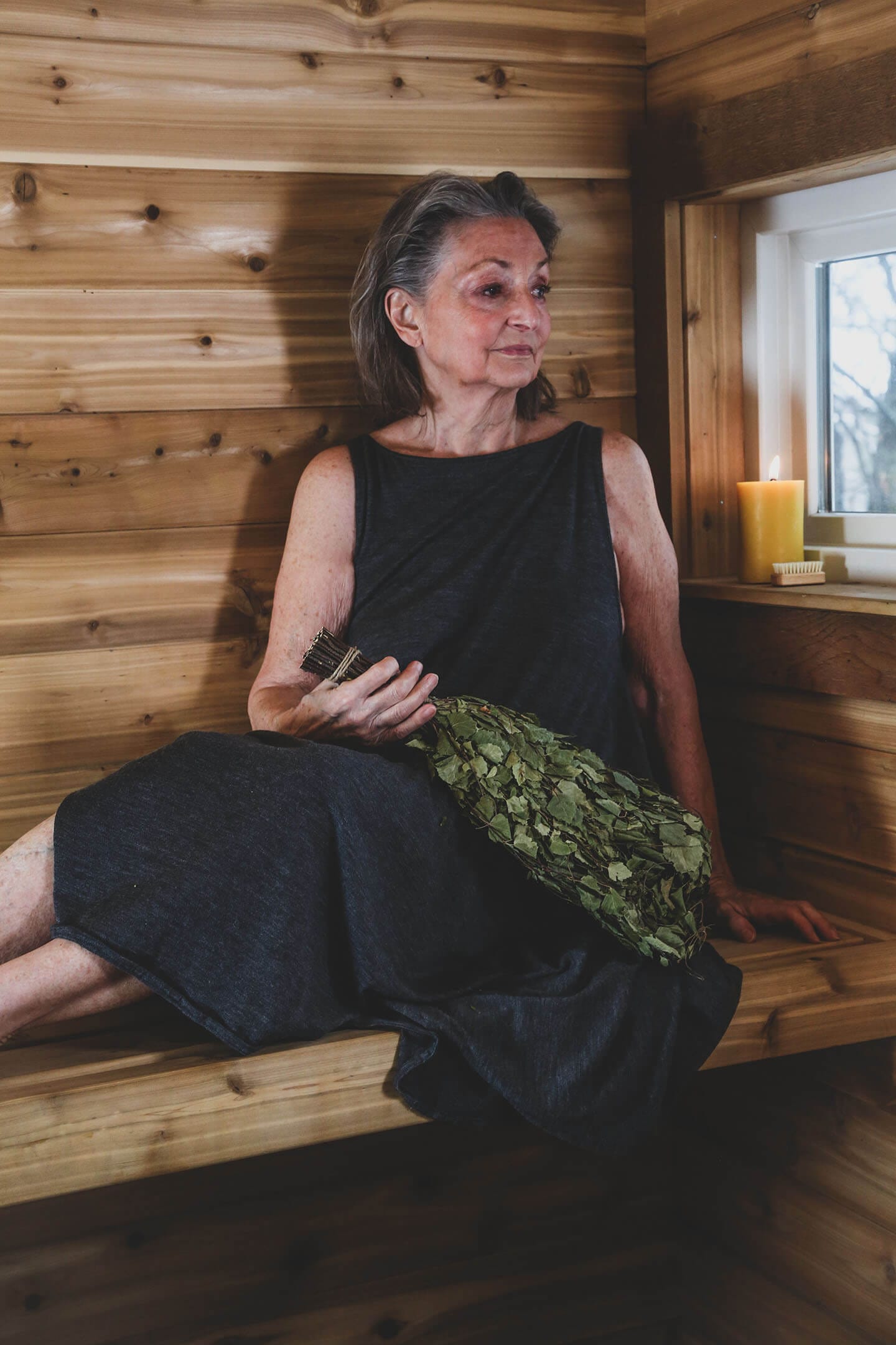 Merino wool sauna dress paired with fresh sauna greenery in a traditional wood sauna setting.