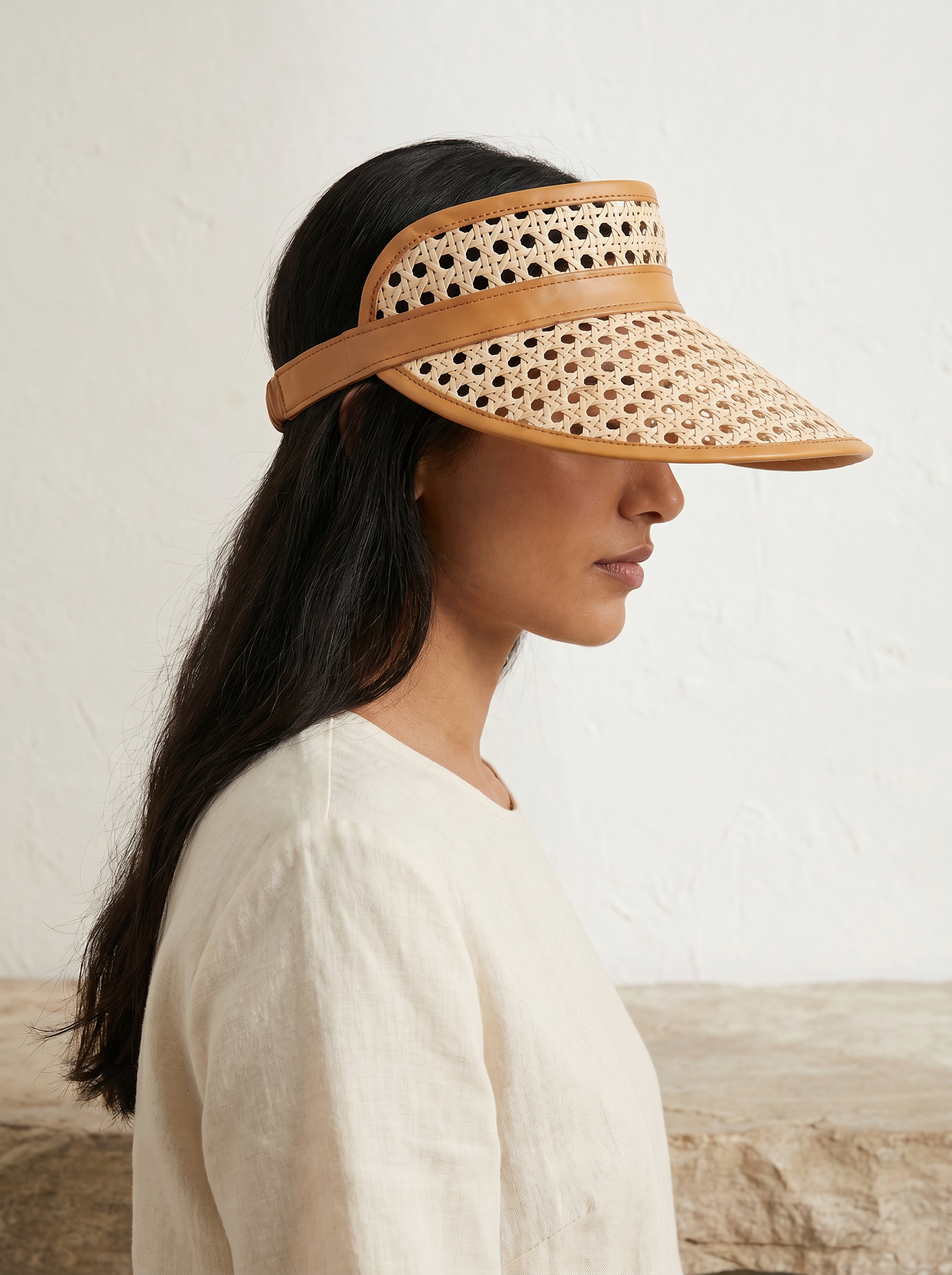 Village Thrive Sumi Leather and Cane Rattan Visor, camel rattan cane with dark leather trim, worn by a model in a white top.