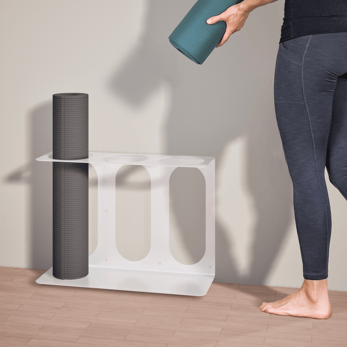 White three-slot bracket holding one gray rolled mat while a barefoot person approaches with a teal roller.