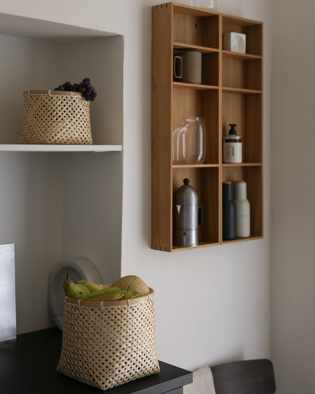 Bamboo baskets used for storage and produce beside a wall-mounted wooden kitchen organizer.
