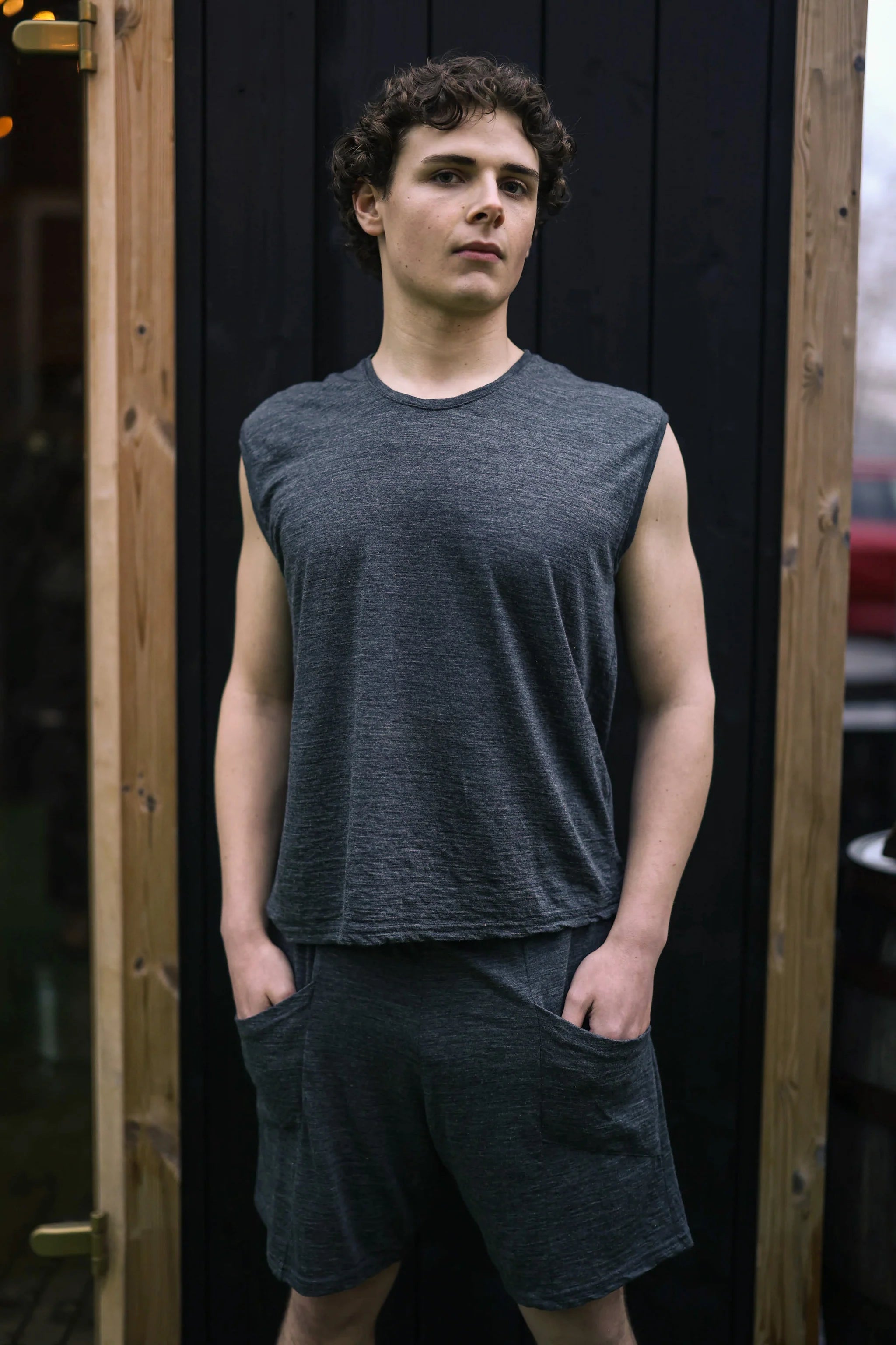 Man wearing a charcoal merino wool sauna tee outside a traditional sauna, showcasing minimalist Finnish-inspired design.