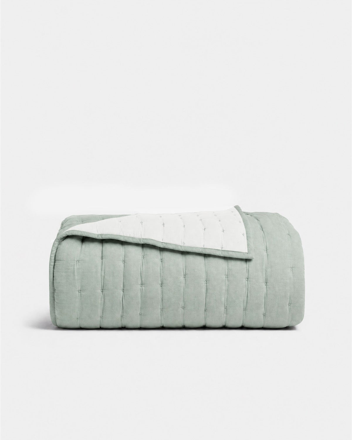 Folded sage green quilt with one corner turned back, showing its pale reverse and neatly bound edge.