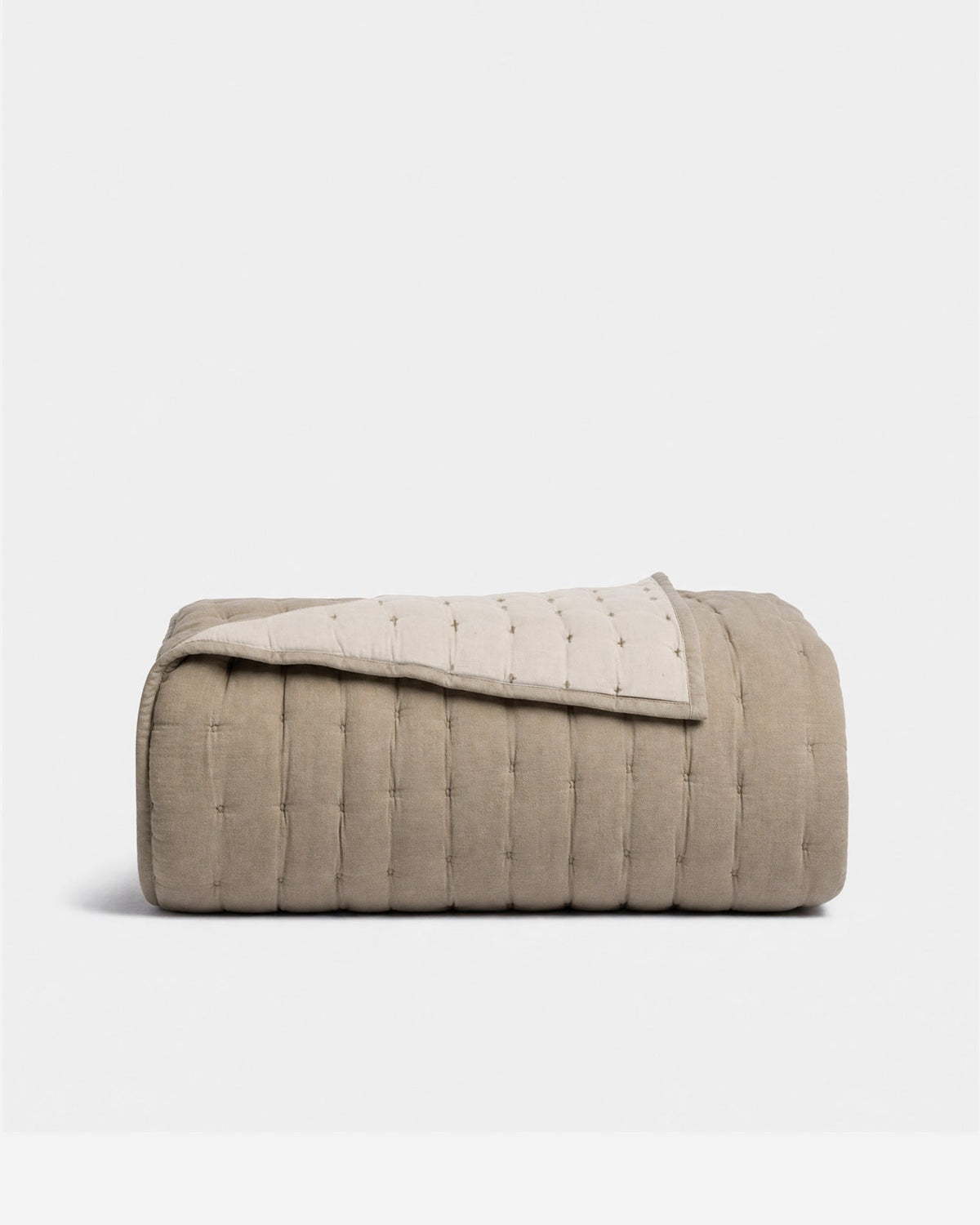 Folded taupe quilt with padded vertical channels and small tufted stitches, with one corner turned back to reveal its cream reverse.