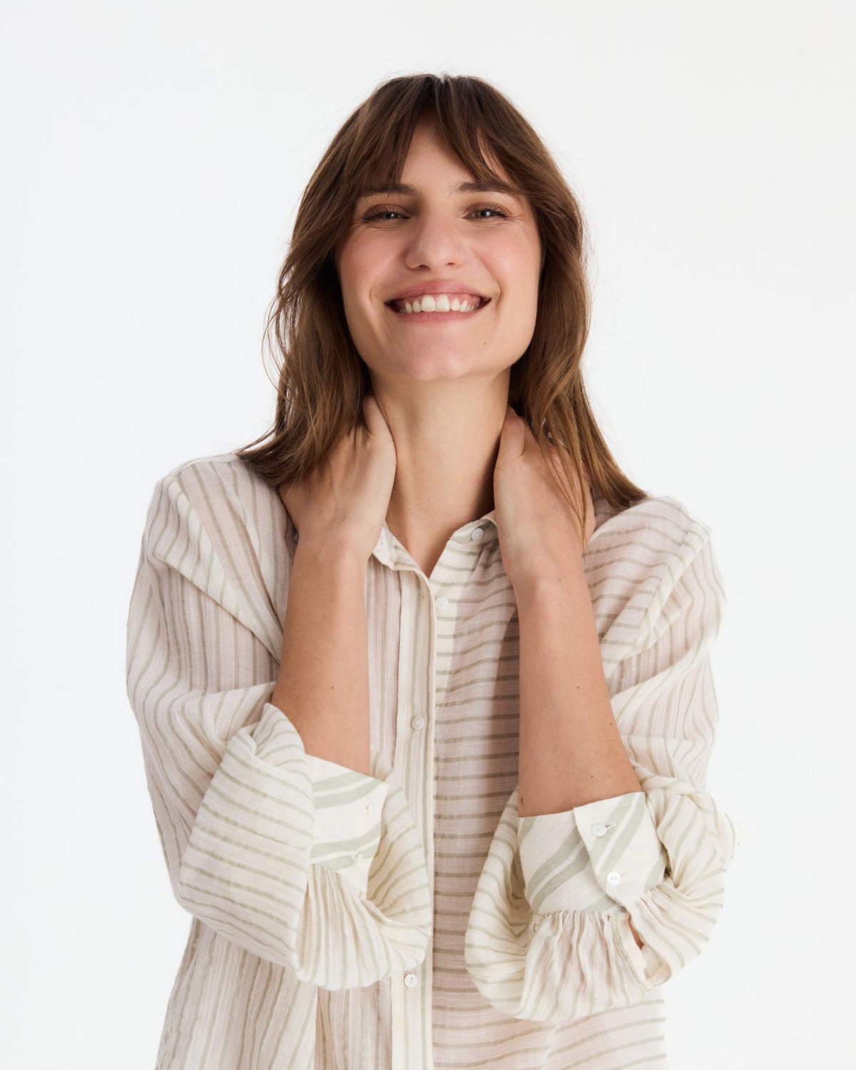 Smiling model holding the shirt’s collar, showing its contrasting stripe panels, buttons, and wide sleeve cuffs.