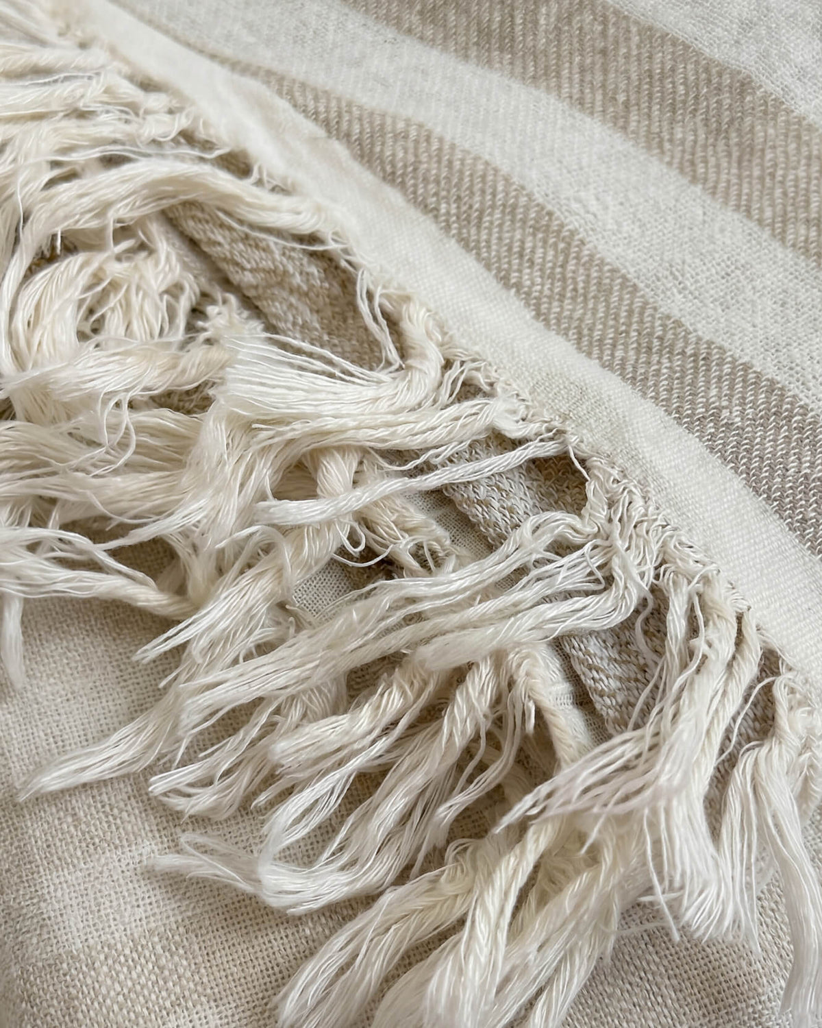 Close-up of the blanket’s woven beige and cream stripes and loosely knotted cream tassels.
