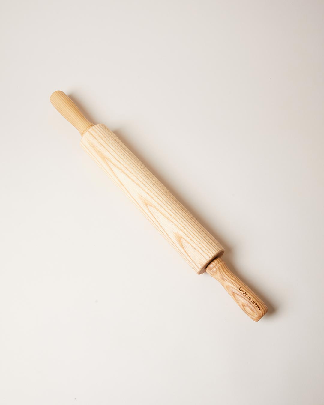 Natural honey-colored ash rolling pin displayed diagonally, showing prominent flowing wood grain along the barrel and handles.